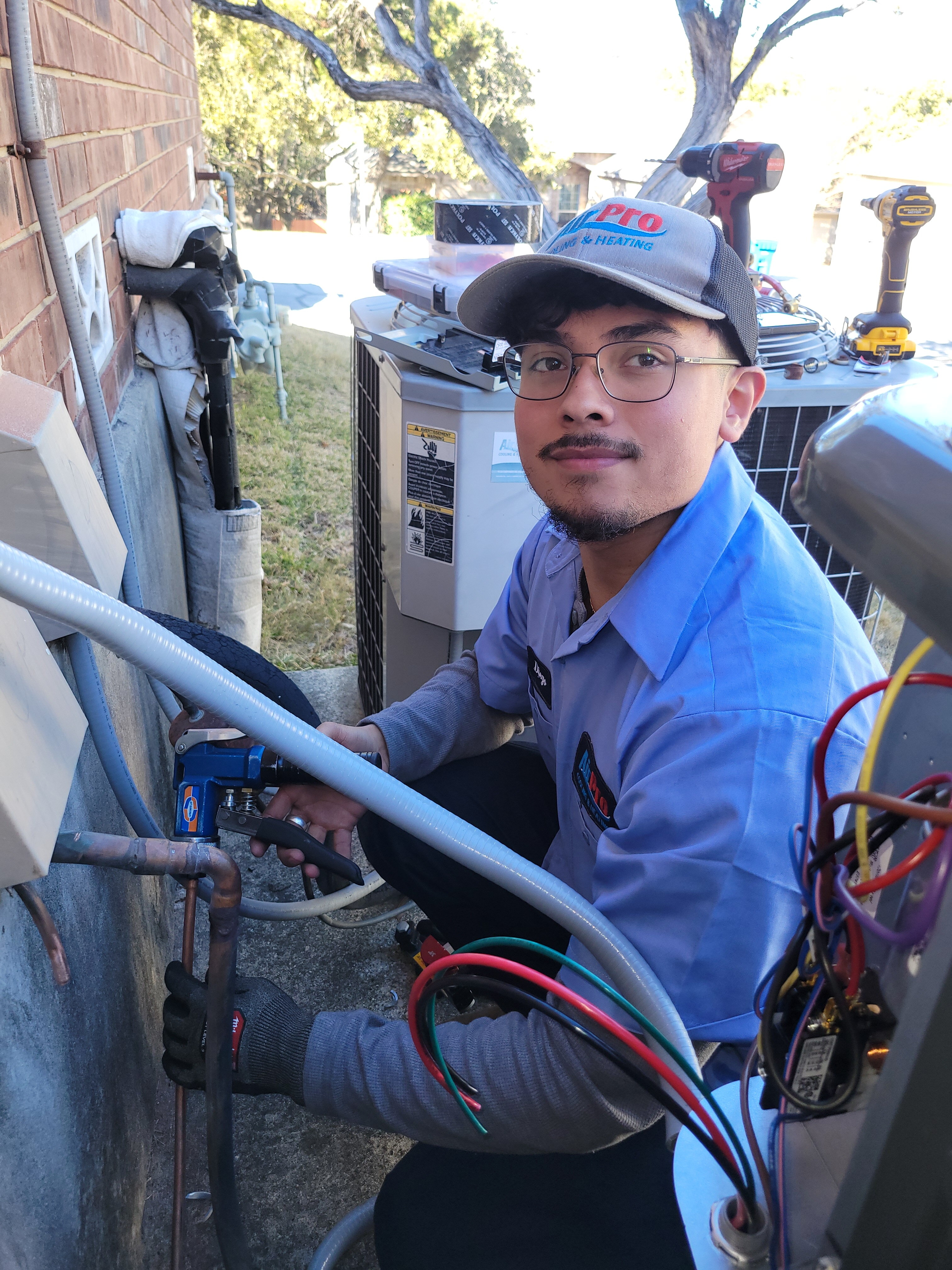 AirPro technician in uniform working on the refrigerant lines of an AC unit