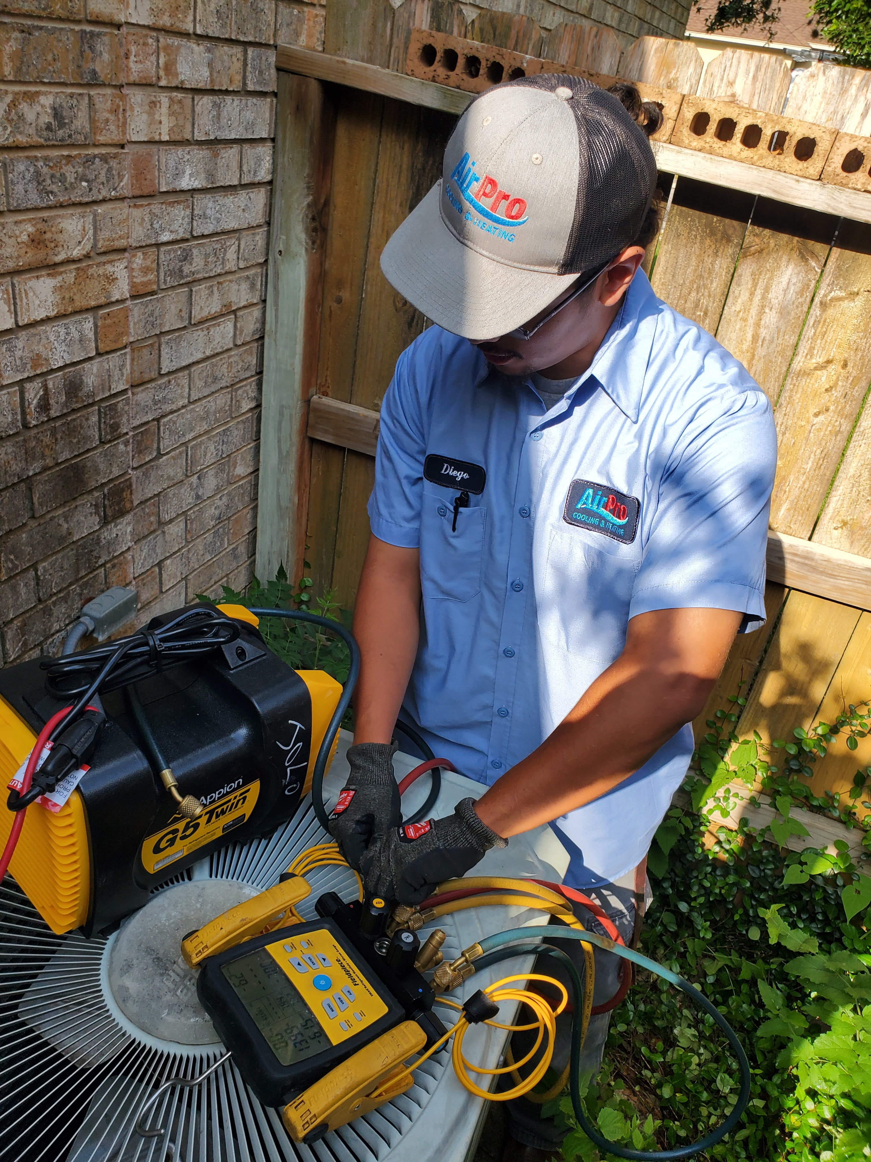 AirPro technician Diego servicing an outdoor AC condenser with vacuum pump and gauges