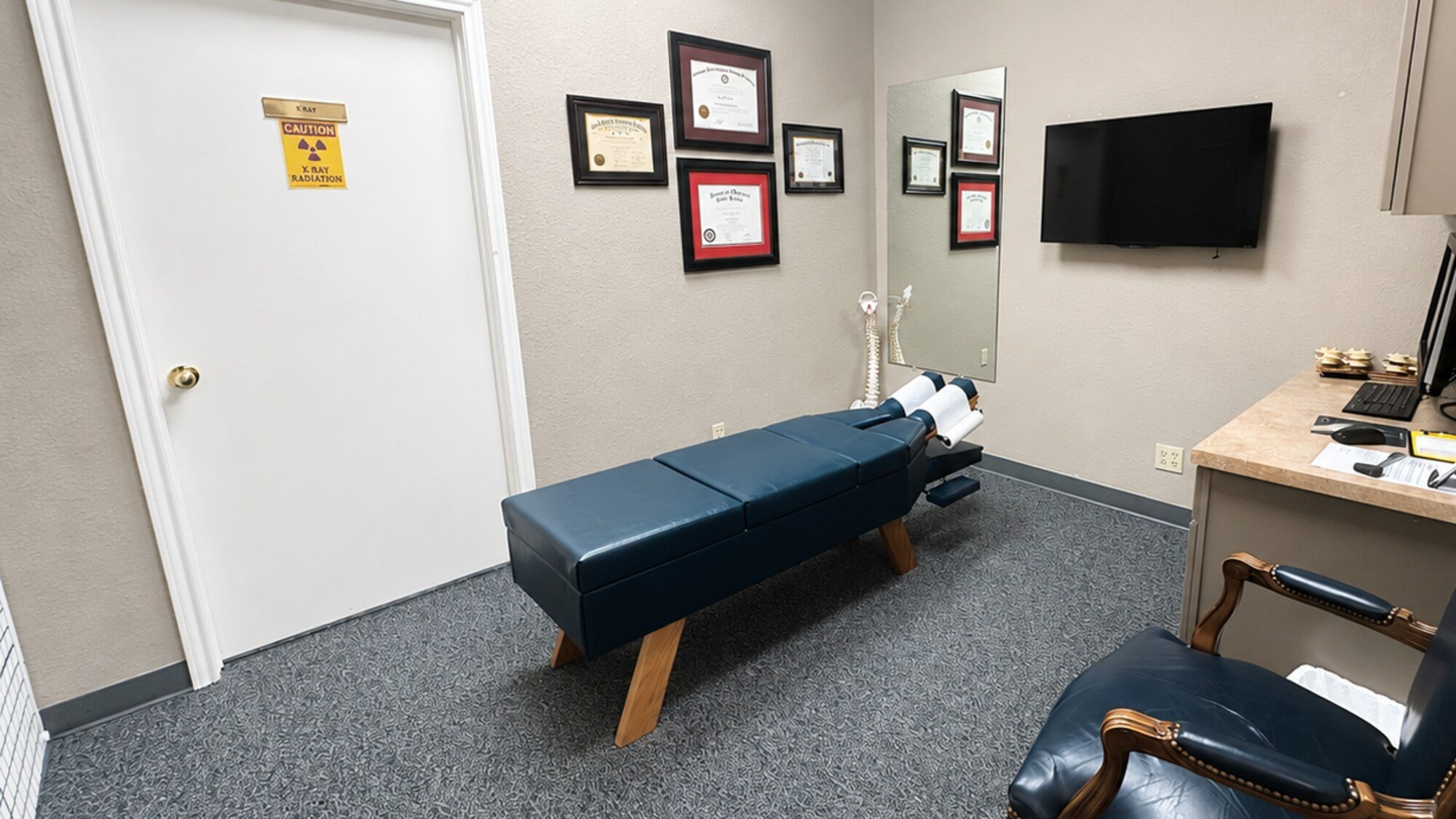 A treatment room at Bandera Chiropractic, with the navy adjusting table, mirror and doctor's desk